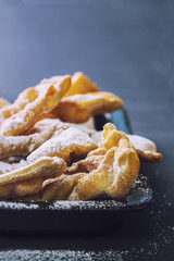 Fresh faworki sprinkled with powdered sugar on a dark table