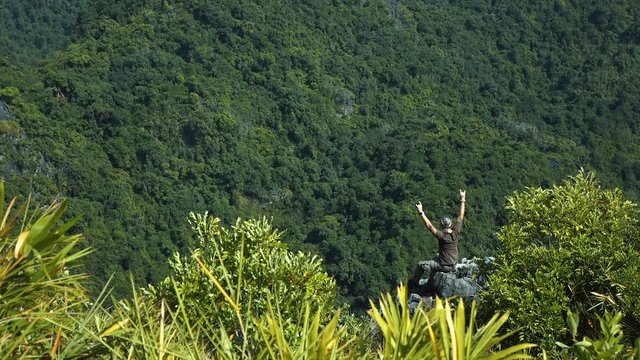 Man sitting on the top of the rock and rising his hands admiring beautiful views. Wide shot. Full HD slow motion stock footage.
