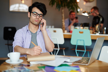 Pensive young man calling while concentrating on creative work