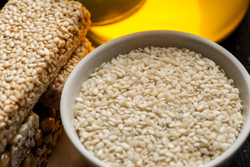 Sesame seeds in a white ceramic bowl and few brittle with honey jar, closeup shot
