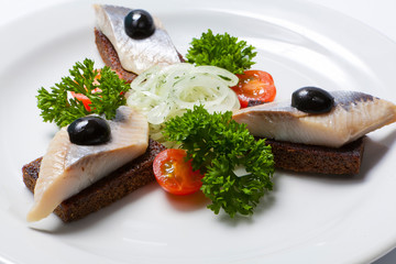 Sliced black bread and herring on a white plate