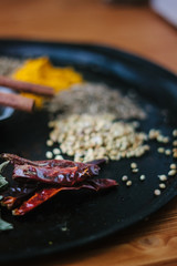 Chili pepper on black metal surface surrounded by spices.