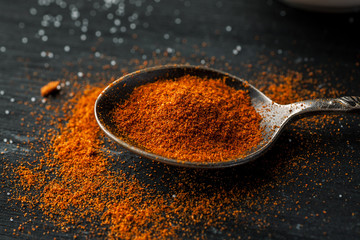 Metal spoon with paprika powder on a black wooden table