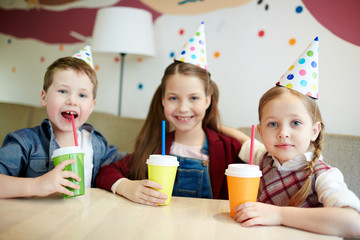 Happy children in birthday caps having soda in cafe