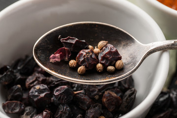 Dry barberry berries with coriander seeds in metal spoon macro shot