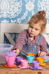 little girl playing toy baby dishes at home