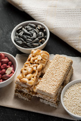 Peanut and sesame brittle stacked on a piece of paper with ceramic bowls with same ingredients, vertical