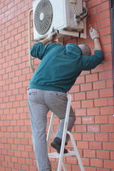 Man standing on ladders and repair of air conditioning system.