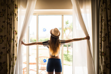 Fototapeta na wymiar girl in hat opens the curtains, Summer morning in hotel room