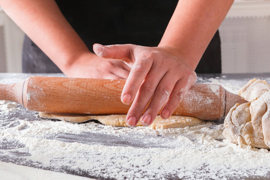 Baking concept. Hands roll dough on black background.