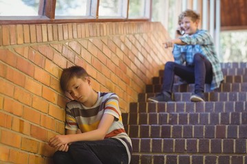 School friend bullying a sad boy in school corridor