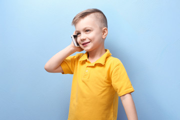 Cute little boy talking by mobile phone on color background