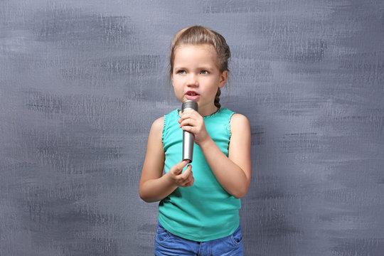 Cute little girl with microphone on color background