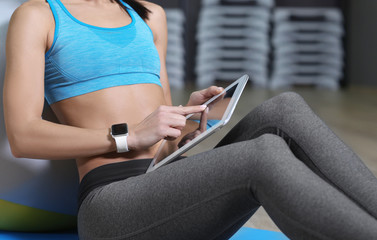 Young woman with tablet computer and fitness tracker in gym