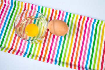 Raw chicken egg in glass bowl with egg on multicolored  tray isolated on white background