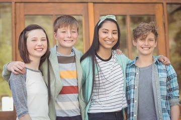 Portrait of happy students standing with arms around in campus