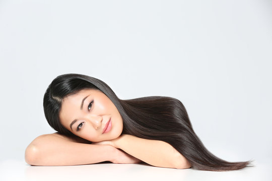 Beautiful Asian woman with long straight hair on light background