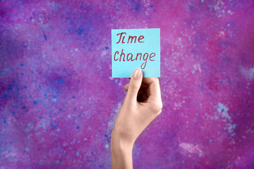 Female hand holding card with text TIME CHANGE on color background