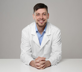 Young handsome pharmacist standing at table on grey background