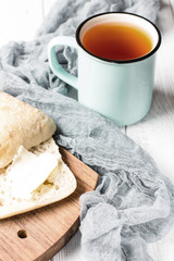 A cup of tea and ciabatta with butter on a white wooden background, soft selective focus, vertical 
