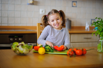 Cute girl of younger school age cuts vegetables and greens for salad.