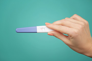 Pregnancy test in hand on color background