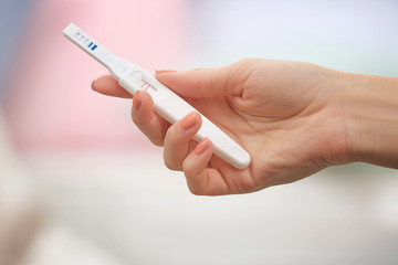 Pregnancy test in hand on blurred background of living room