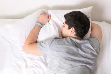 Young man with sleep tracker resting in bed at home
