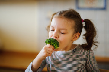 Cute fair-haired girl eats fresh broccoli.