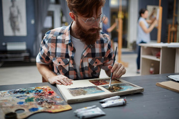 Man sitting by table and painting on small canvas