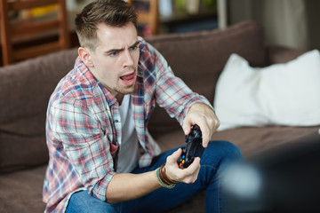 Portrait emotional adult man playing video game holding wireless controller and  opening mouth...