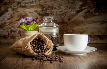 Coffee in sack and white cup, decorate with glass jar, flower and blur old wall for background