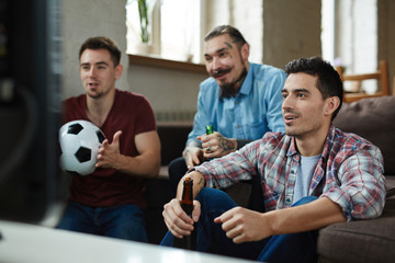 Naklejka premium Group of friends watching football match on TV while sitting on couch and drinking beer