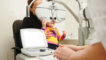 High technology in ophthalmology - optometrist in clinic checking little girl's vision - children's...