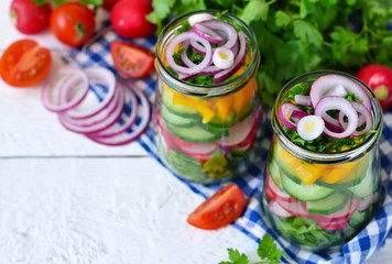 Vegetable salad with spinach and red onions in a glass jar on a white background