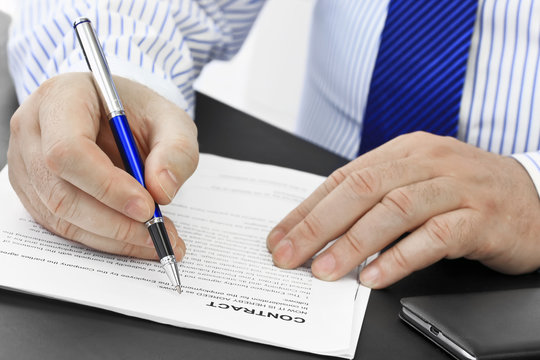 Businessman with pen analyzing contract at desk in the office