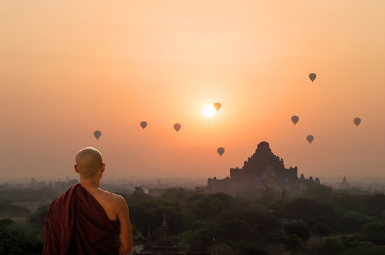 Monk looking at hot air balloons at sunrise at Bagan temple in Burma, Myanmar