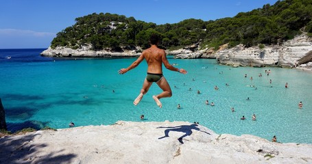 Chico saltando sobre playa de agua cristalina
