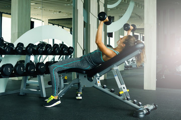 Fototapeta na wymiar Woman working out with dumbbells in gym
