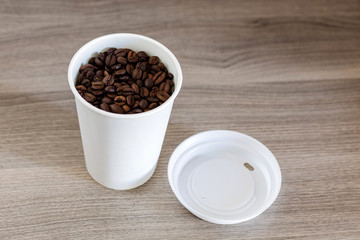 Paper cup and coffee beans on the wooden background