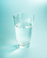 A glass of pure cool water on a textured light blue background close-up with beautiful light and highlights.