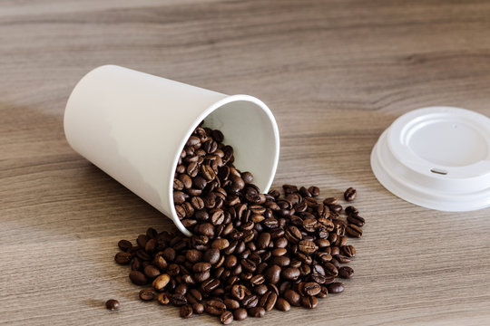 Paper cup and coffee beans on the wooden background