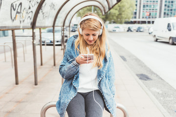 Young blonde beautiful woman listening music with head phones and smart phone hand hold - music,...