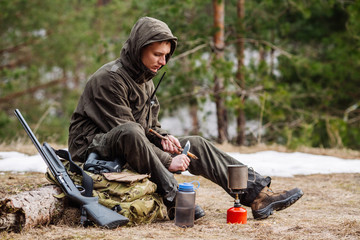 male hunter preparing food with a portable gas burner in a winter forest.
