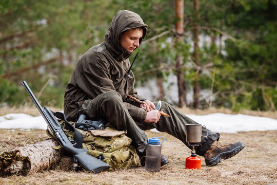 male hunter preparing food with a portable gas burner in a winter forest.