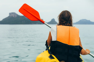 Back view of young woman kayaking in sea on background of mountains