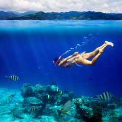 Underwater shoot of a young woman snorkeling in a tropical sea and coast mountain splitted by waterline