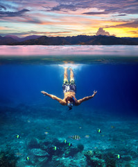 Underwater shoot of a young man snorkeling in a tropical sea and colorful sunset splitted by waterline