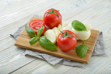 Mozzarella and tomato with basil leaves on a white wooden background