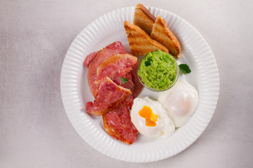 Bacon, poached eggs, mashed peas and toasts on white plate. Grilled rashers and eggs